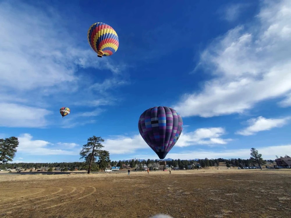 Three colorful hot air balloons in a clear blue sky over an open field.
