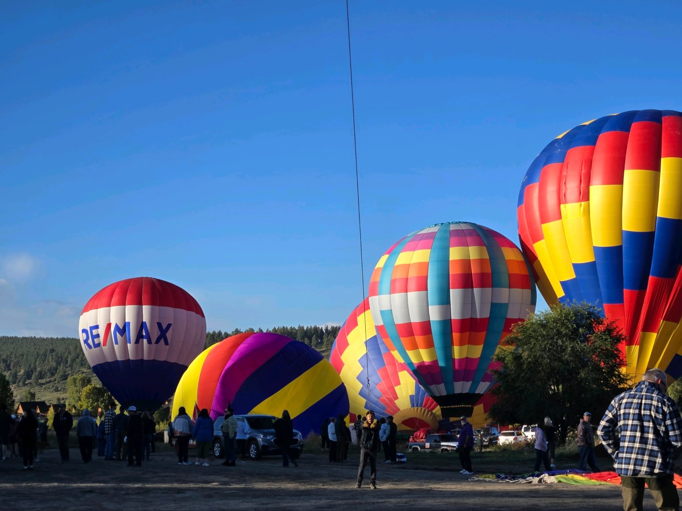 Colorful hot air balloons on the ground with people around on a clear day.
