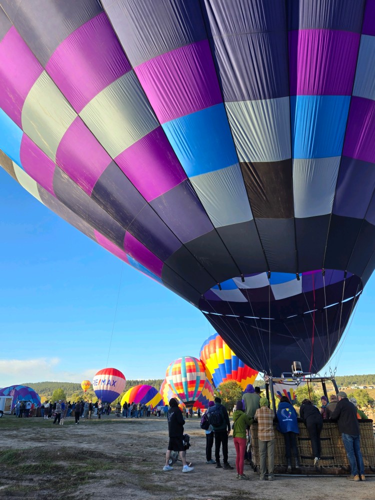Colorful hot air balloons preparing for lift-off at a festival with people gathered around.