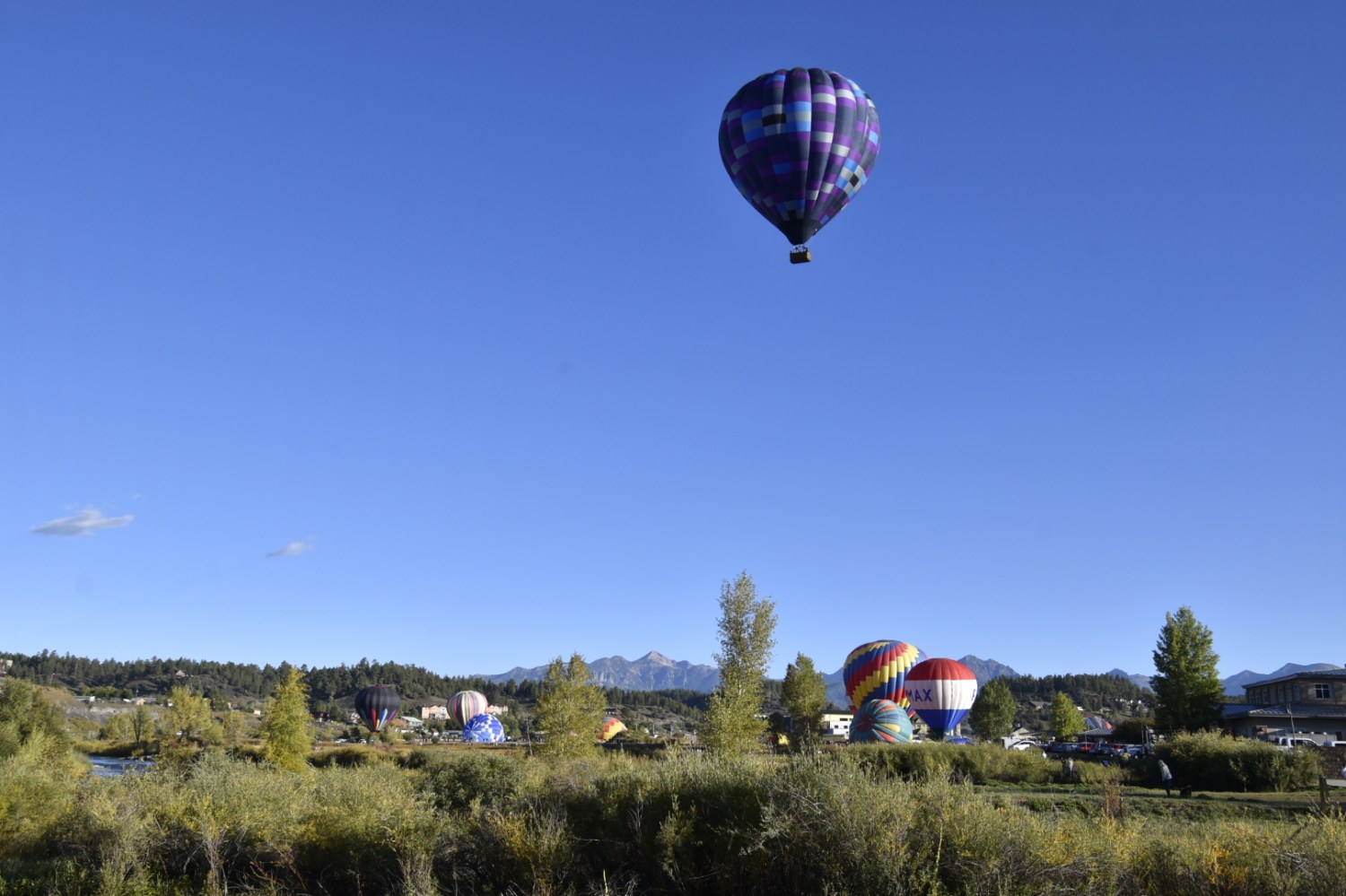 A colorful hot air balloon floats above a scenic landscape with mountains and trees.