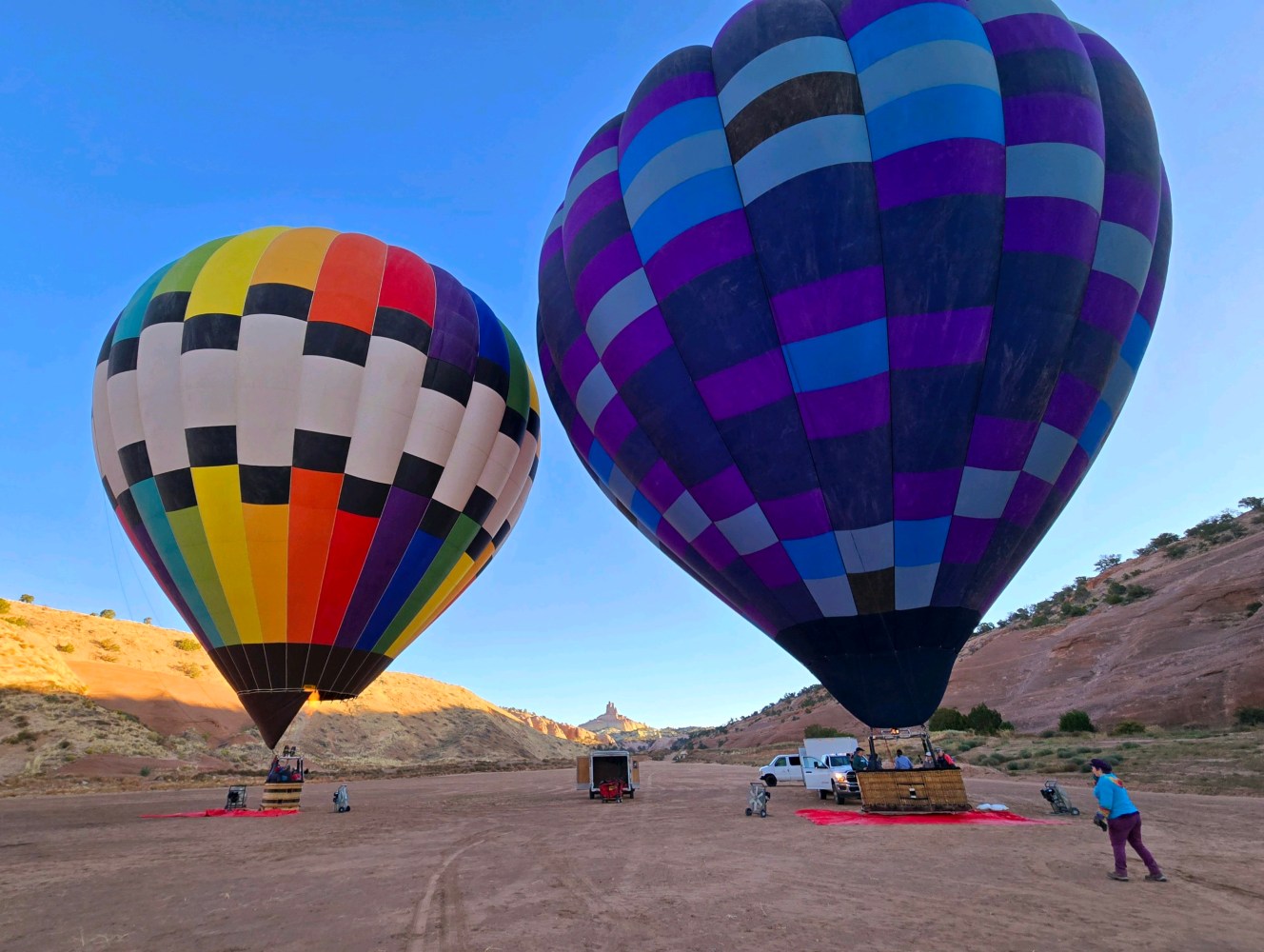 Two vibrant hot air balloons on a desert landscape with clear blue sky.