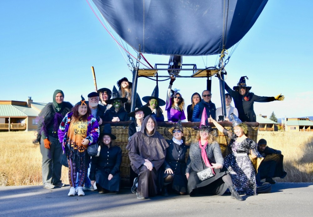 Group in Halloween costumes poses with a hot air balloon on a sunny day.