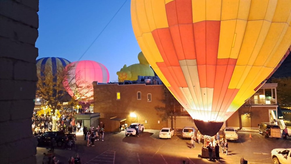 Hot air balloons glow at night above a crowd in a town square.