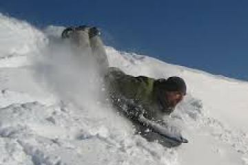 Person sledding headfirst down a snowy slope on a clear day.